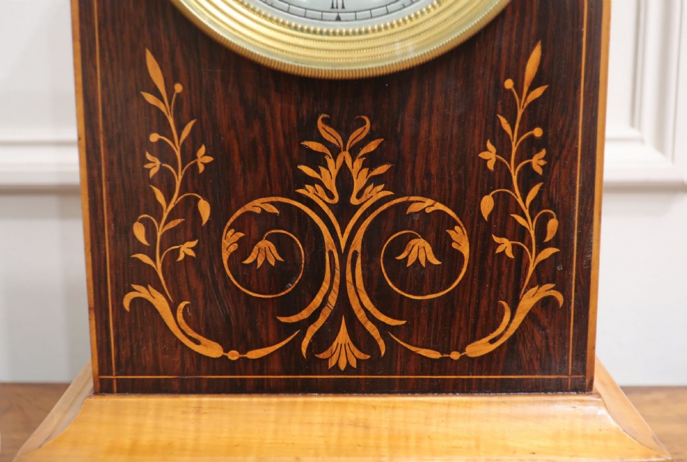 A nineteenth-century rectangular dark rosewood mantel clock featuring foliate marquetry inlay, a brass-rimmed circular dial with Roman numerals, and a stepped plinth base. View IV