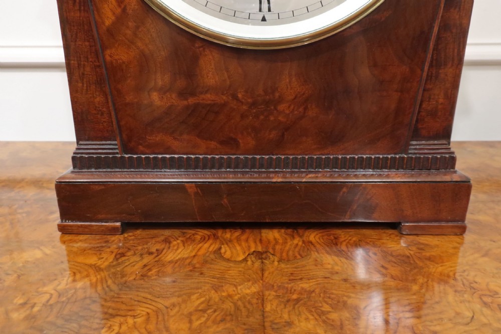 A Georgian flame mahogany bracket clock featuring a circular white dial with Roman numerals, a pointed architectural pediment, and brass side frets. View VI