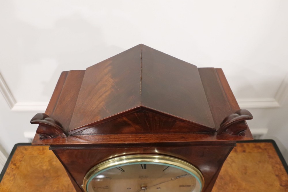 A Georgian flame mahogany bracket clock featuring a circular white dial with Roman numerals, a pointed architectural pediment, and brass side frets. View VIII