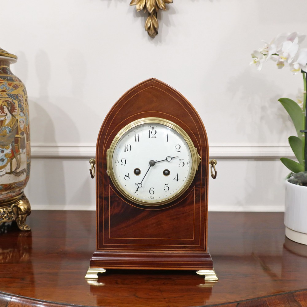A French Belle Epoque arched mahogany mantel clock featuring a white enamel dial, brass bezel, and fine stringing inlay.