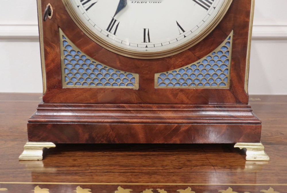 A Regency mahogany bracket clock featuring brass mounts, a top handle, fishscale brass side frets, and a circular white dial signed Rives Bedford. View VI