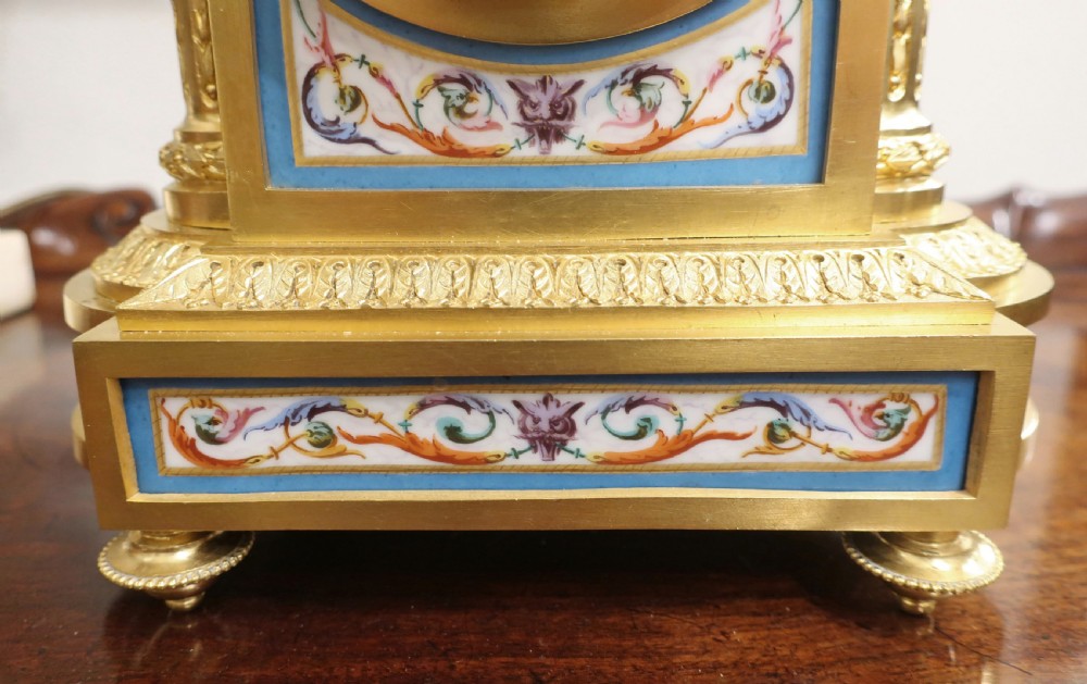 An antique French gilt bronze mantel clock featuring a central urn finial, fluted side columns, and hand-painted light blue porcelain panels with Roman numeral markers. View V