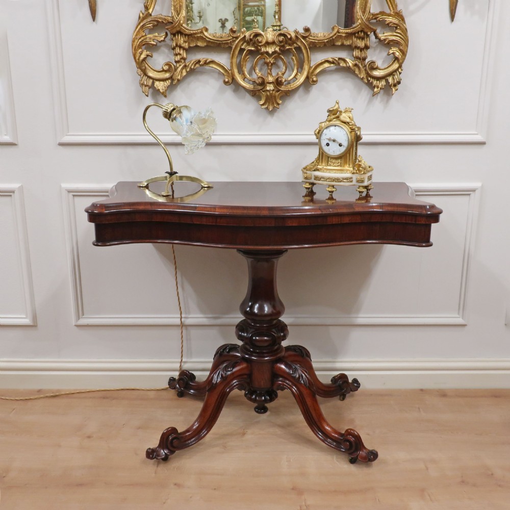 A Victorian dark brown rosewood side table featuring a serpentine top, central turned column, and four carved scroll legs.