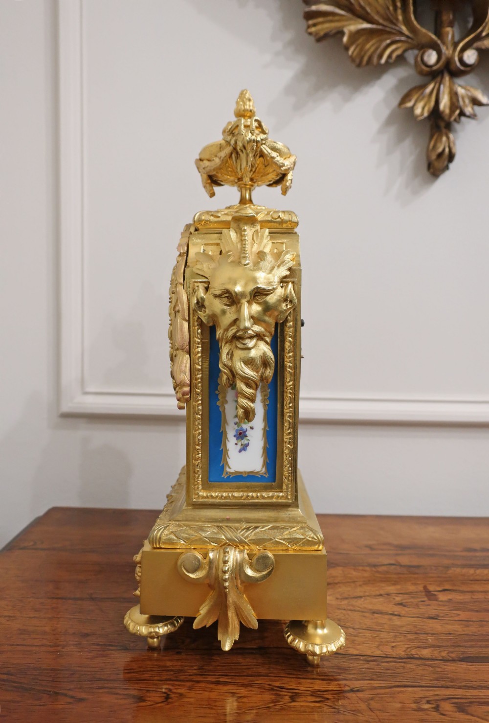 A French gilt bronze mantel clock featuring hand-painted blue porcelain panels, classical urn finial, and Roman numeral dial centre. View XIII