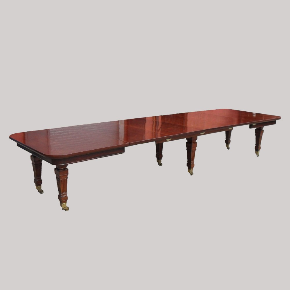 A long Victorian mahogany imperial extending dining table with a polished surface finish, fluted turned legs, and brass castors.