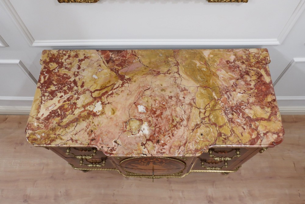 A French Louis XVI style chest of drawers featuring detailed wood marquetry, gilt-bronze mounts, tapering fluted legs, and a fitted marble top. View IX