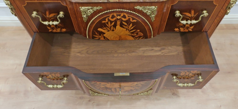 A French Louis XVI style chest of drawers featuring detailed wood marquetry, gilt-bronze mounts, tapering fluted legs, and a fitted marble top. View XVII