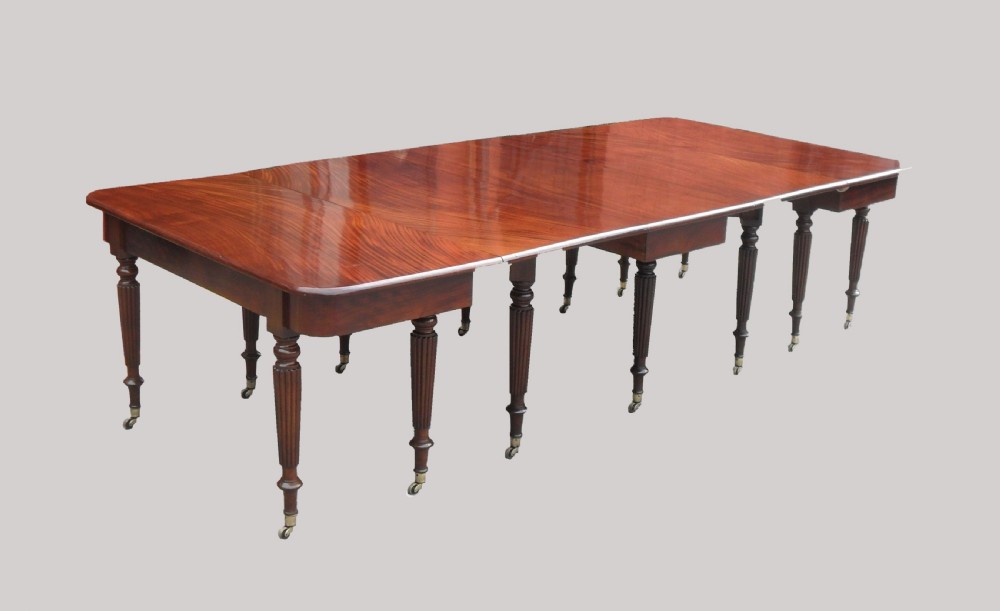 A long Georgian mahogany extending dining table featuring a polished rectangular top with rounded corners supported by reeded legs on brass castors.