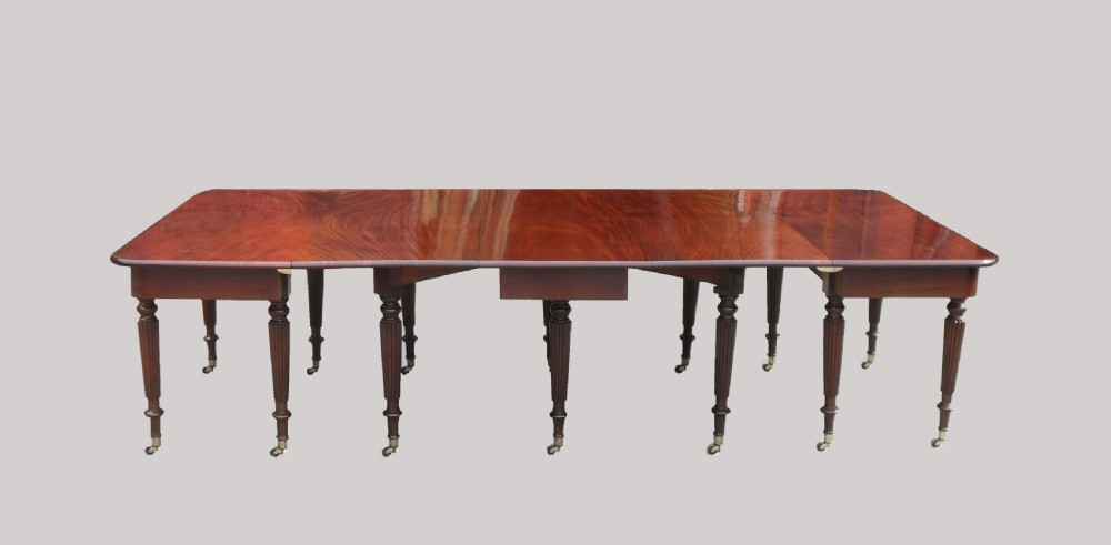 A long Georgian mahogany extending dining table featuring a polished rectangular top with rounded corners supported by reeded legs on brass castors. View III