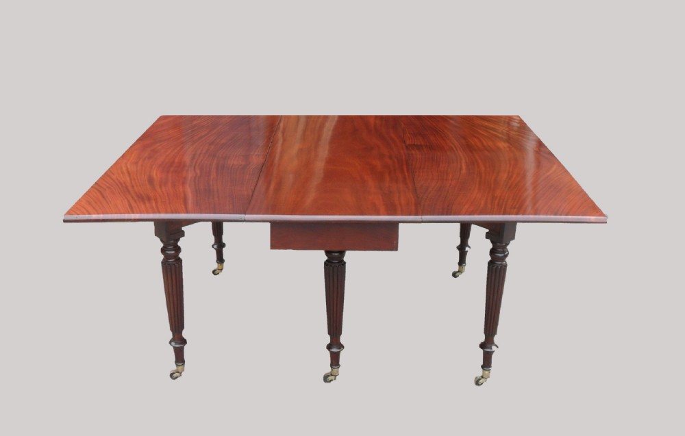 A long Georgian mahogany extending dining table featuring a polished rectangular top with rounded corners supported by reeded legs on brass castors. View IV