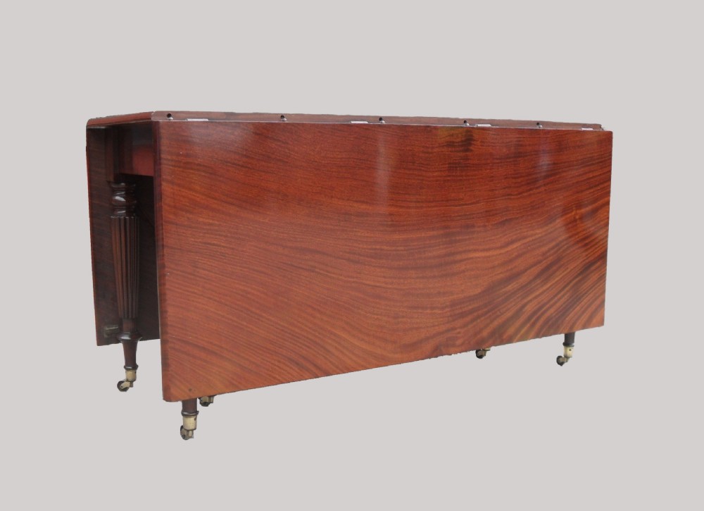 A long Georgian mahogany extending dining table featuring a polished rectangular top with rounded corners supported by reeded legs on brass castors. View V