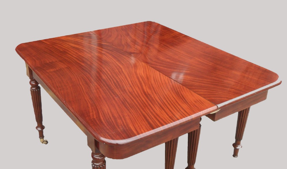 A long Georgian mahogany extending dining table featuring a polished rectangular top with rounded corners supported by reeded legs on brass castors. View IX