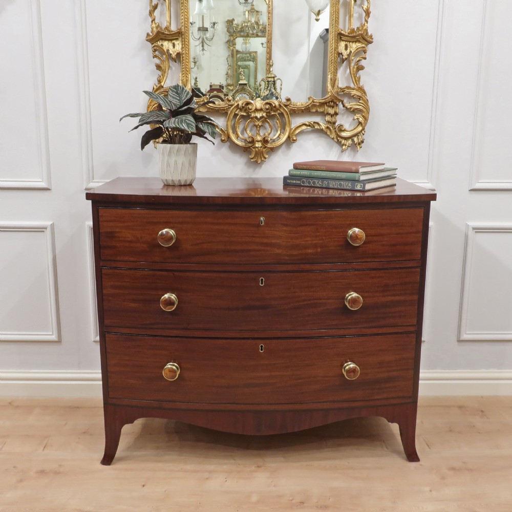A Georgian bow-fronted mahogany chest of drawers featuring three graduated drawers with circular brass knob handles and splayed bracket feet.