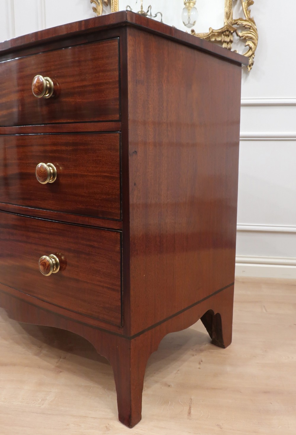 A Georgian bow-fronted mahogany chest of drawers featuring three graduated drawers with circular brass knob handles and splayed bracket feet. View XII