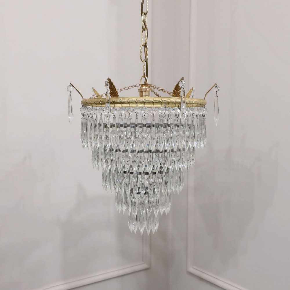 A five-tiered Art Deco chandelier featuring concentric rings of clear glass droplets suspended from a decorative gilt brass rim with a hanging chain.