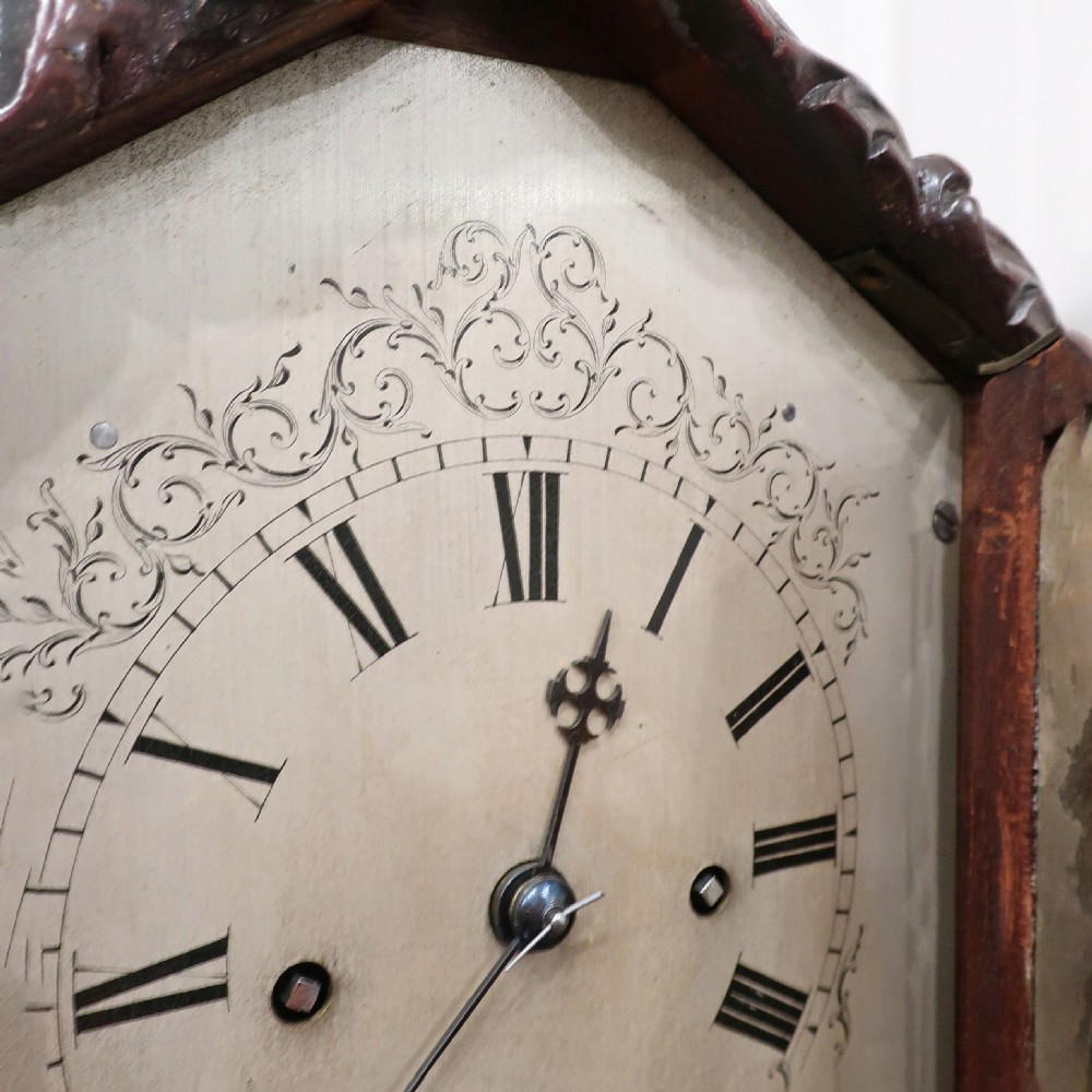 An early Victorian mahogany library clock featuring a heavily carved leafy frame, Roman numeral dial face, and stepped side moulding. View IV