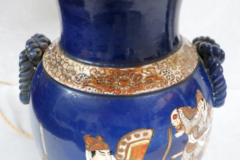 A pair of cobalt blue Japanese Satsuma porcelain vase table lamps with painted warrior figures, brass fittings, dark wood bases, and a pleated fabric shade. View VI