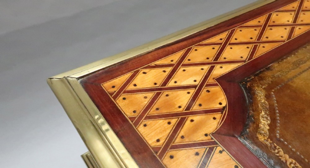 A Victorian writing table featuring geometric parquetry inlay, a brown leather inset top, gilt-brass edge moulding, two frieze drawers, and square tapered legs on castors. View V
