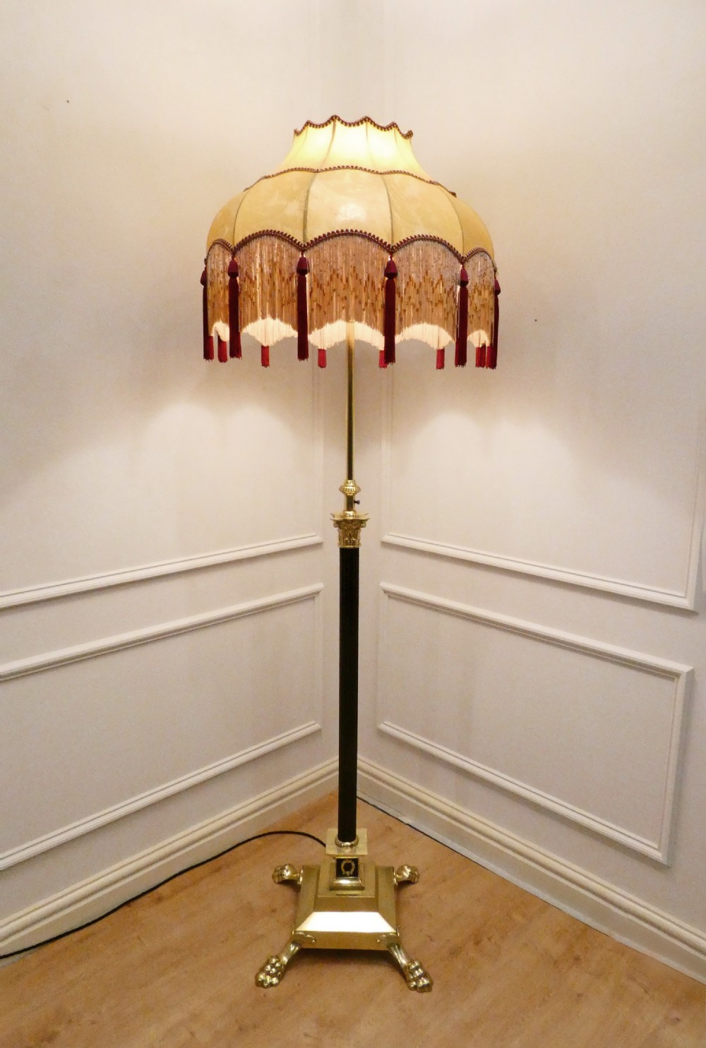 A Victorian brass standard floor lamp featuring a Corinthian capital, stepped base with claw feet, and a fringed cream shade with red tassels. View VIII