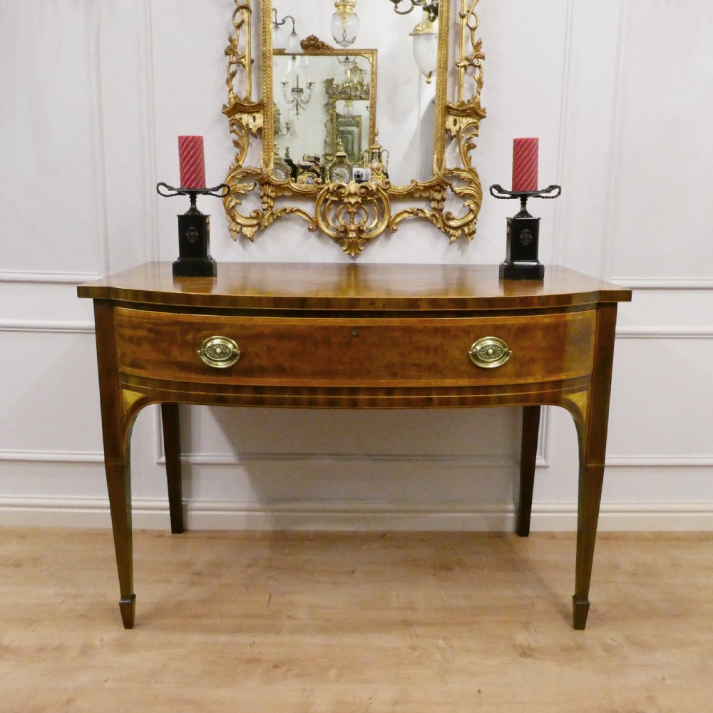 A Georgian mahogany bowfront side table featuring a single drawer with two oval brass handles and square tapered legs.