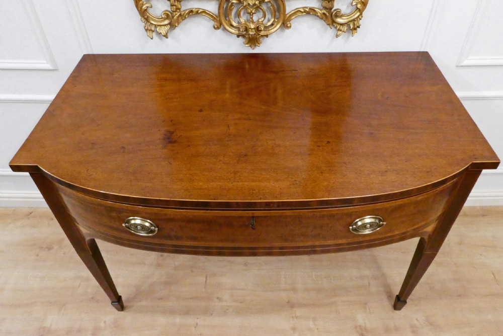 A Georgian mahogany bowfront side table featuring a single drawer with two oval brass handles and square tapered legs. View VI