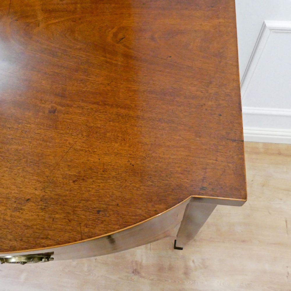 A Georgian mahogany bowfront side table featuring a single drawer with two oval brass handles and square tapered legs. View VII