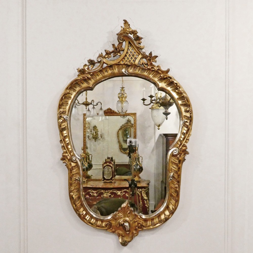 A French Rococo style wall mirror featuring a carved gold leaf frame decorated with acanthus leaf motifs, C-scrolls, and a lattice cartouche crest.