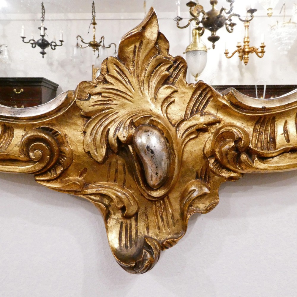 A French Rococo style wall mirror featuring a carved gold leaf frame decorated with acanthus leaf motifs, C-scrolls, and a lattice cartouche crest. View II