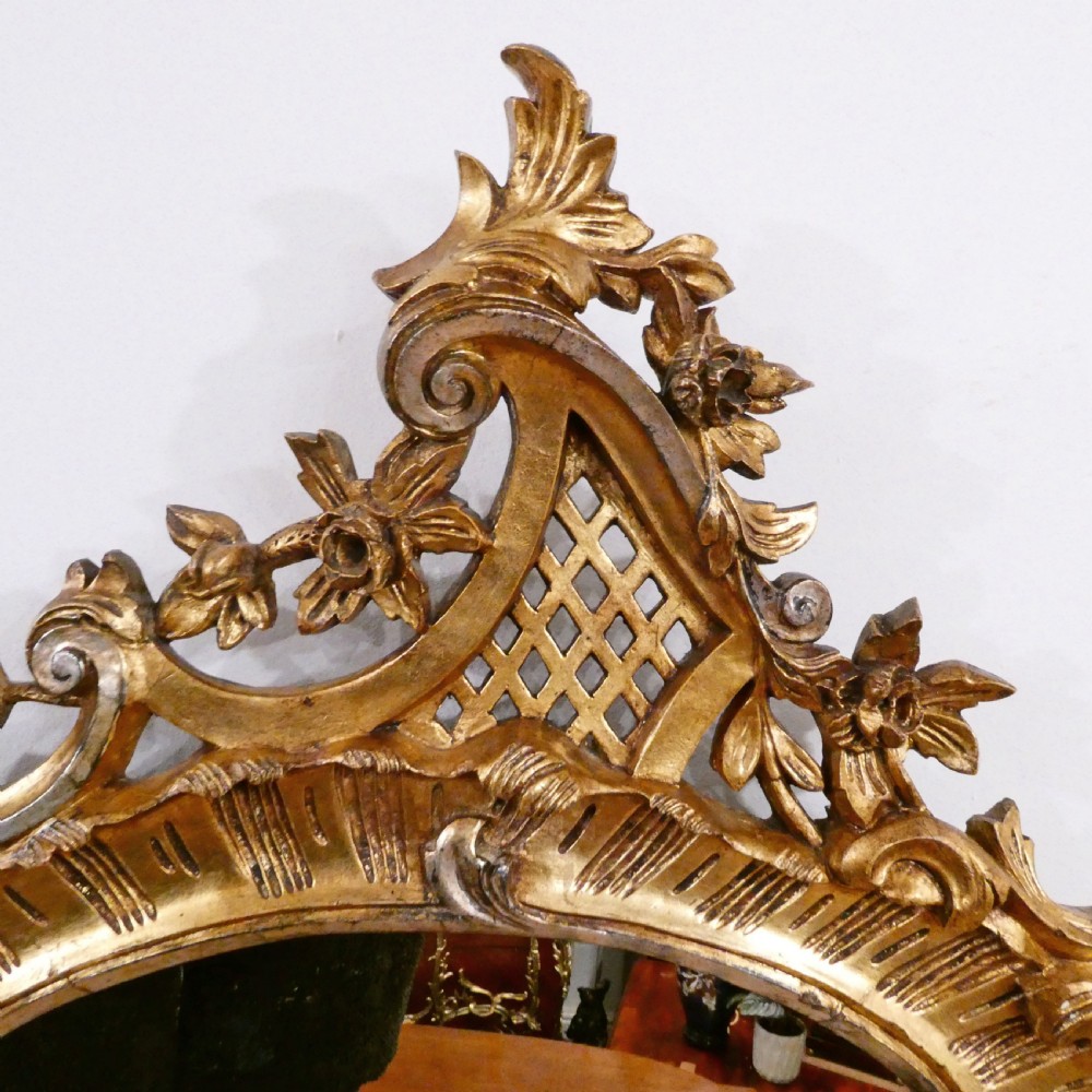 A French Rococo style wall mirror featuring a carved gold leaf frame decorated with acanthus leaf motifs, C-scrolls, and a lattice cartouche crest. View IV