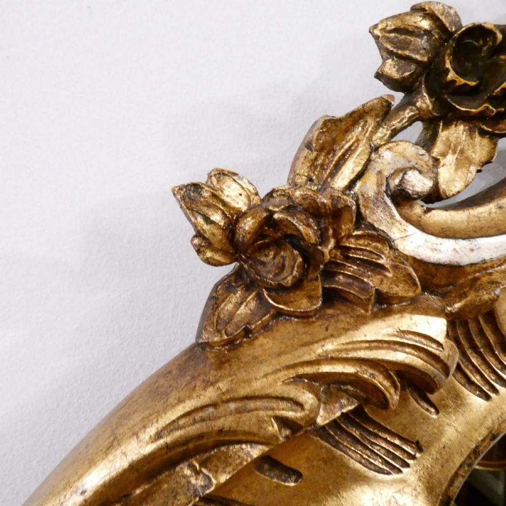 A French Rococo style wall mirror featuring a carved gold leaf frame decorated with acanthus leaf motifs, C-scrolls, and a lattice cartouche crest. View V