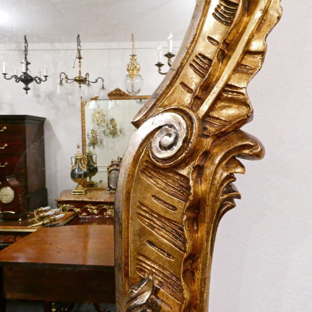A French Rococo style wall mirror featuring a carved gold leaf frame decorated with acanthus leaf motifs, C-scrolls, and a lattice cartouche crest. View IX