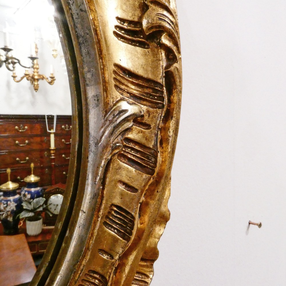 A French Rococo style wall mirror featuring a carved gold leaf frame decorated with acanthus leaf motifs, C-scrolls, and a lattice cartouche crest. View X