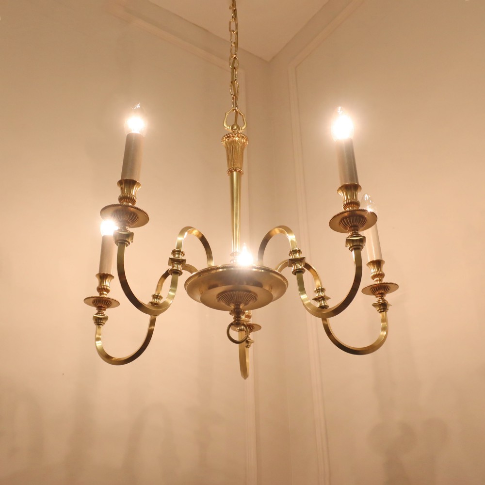 A French gilt bronze five-arm chandelier featuring curved candle arms, reeded collars, and a fluted central stem suspended by a metal chain. View V
