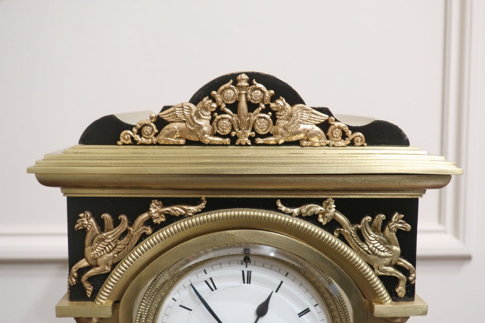 A 19th-century French brass four-glass mantel clock with black decorative corner panels, an enamel dial with Roman numerals, and a visible pendulum movement. View IX
