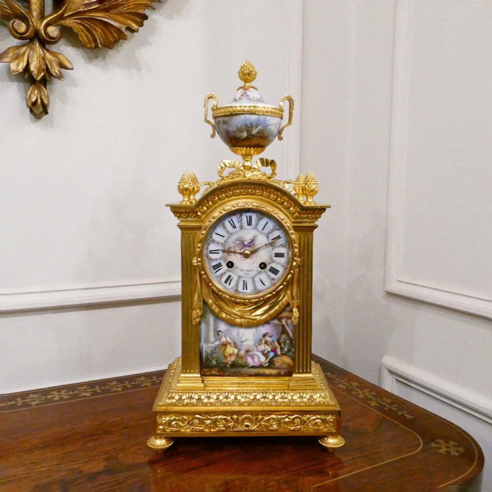 A French Louis XVI style gilt bronze mantel clock featuring a porcelain urn top, hand-painted floral porcelain panels, and Roman numerals on the dial.