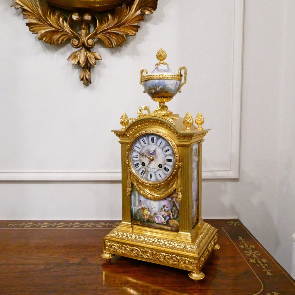 A French Louis XVI style gilt bronze mantel clock featuring a porcelain urn top, hand-painted floral porcelain panels, and Roman numerals on the dial. View II
