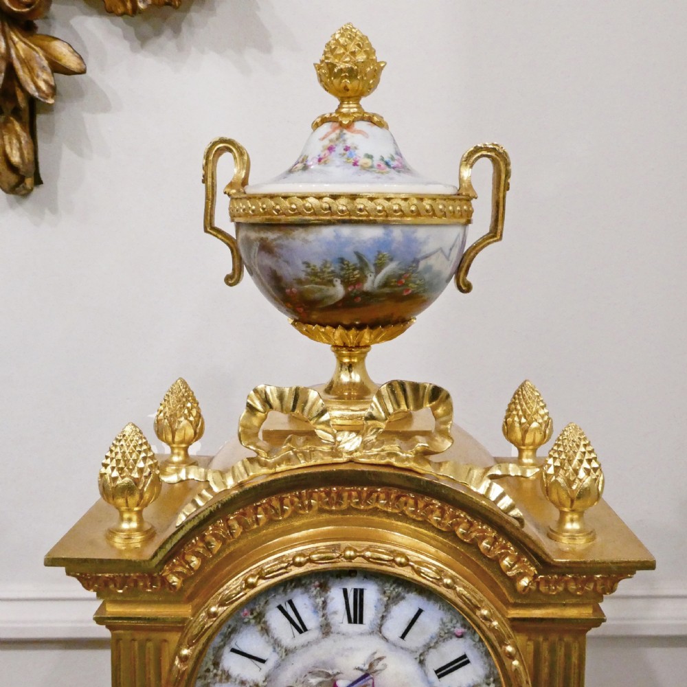 A French Louis XVI style gilt bronze mantel clock featuring a porcelain urn top, hand-painted floral porcelain panels, and Roman numerals on the dial. View VII