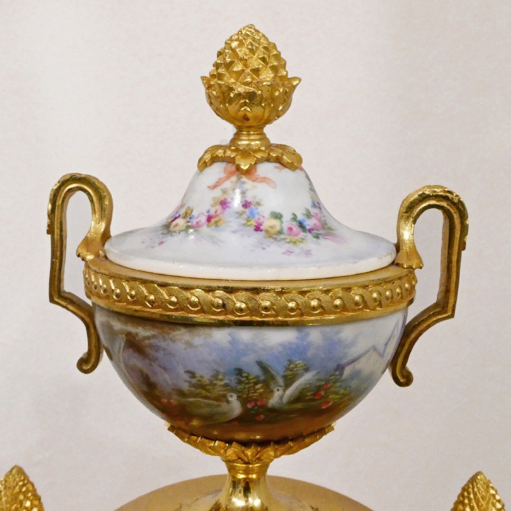 A French Louis XVI style gilt bronze mantel clock featuring a porcelain urn top, hand-painted floral porcelain panels, and Roman numerals on the dial. View VIII