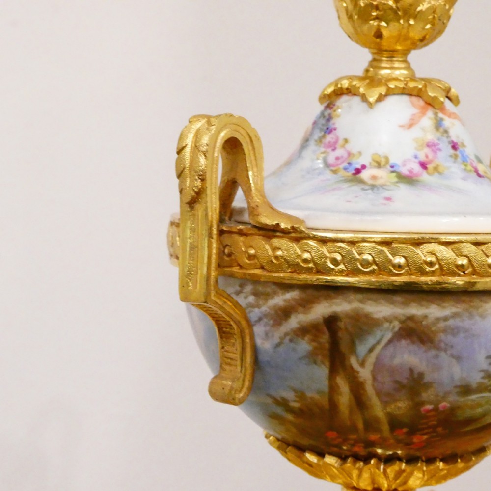 A French Louis XVI style gilt bronze mantel clock featuring a porcelain urn top, hand-painted floral porcelain panels, and Roman numerals on the dial. View IX