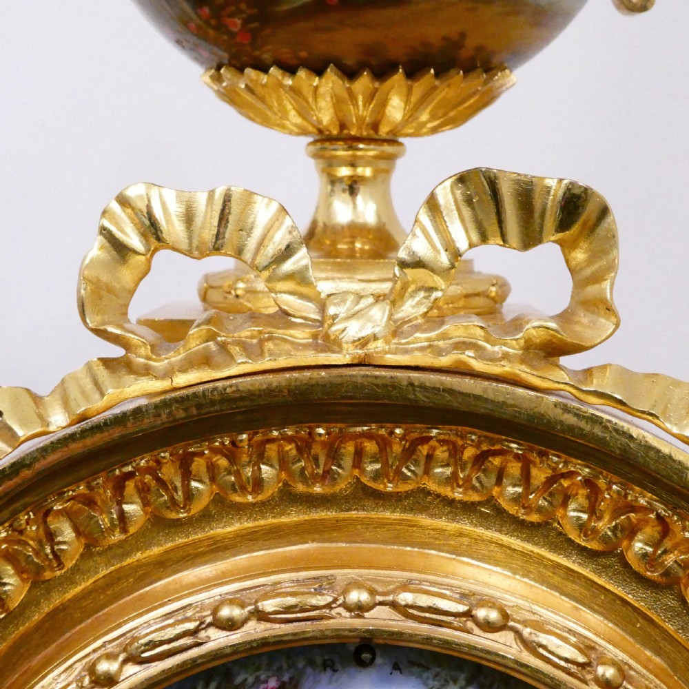 A French Louis XVI style gilt bronze mantel clock featuring a porcelain urn top, hand-painted floral porcelain panels, and Roman numerals on the dial. View XI