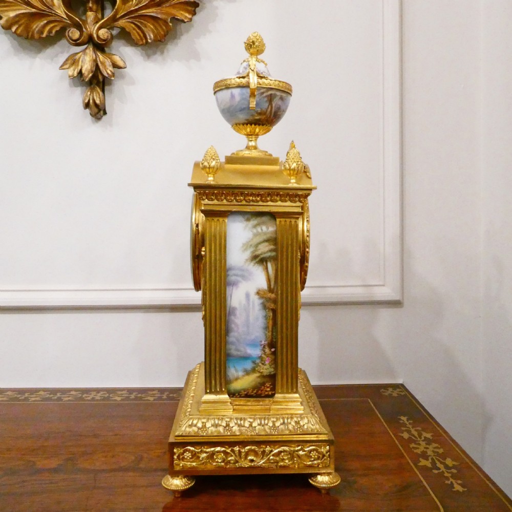 A French Louis XVI style gilt bronze mantel clock featuring a porcelain urn top, hand-painted floral porcelain panels, and Roman numerals on the dial. View XII