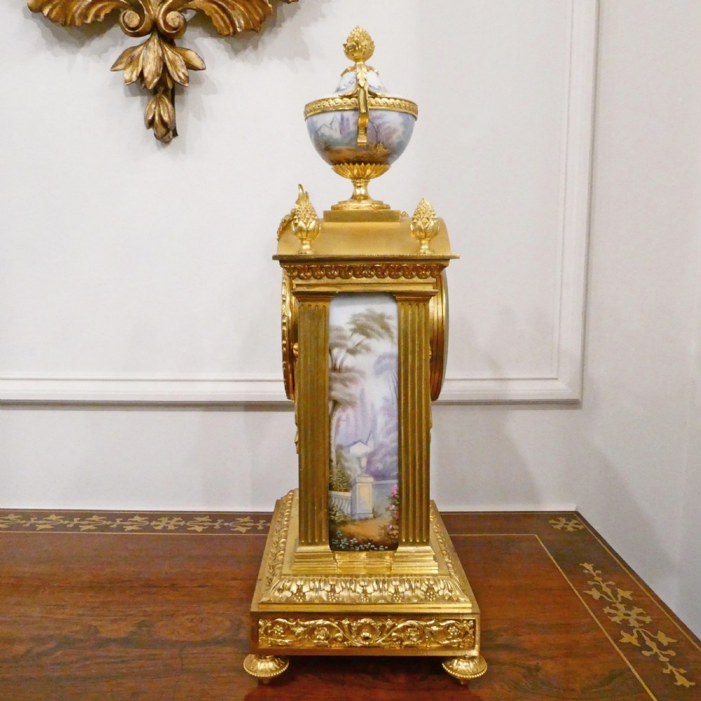 A French Louis XVI style gilt bronze mantel clock featuring a porcelain urn top, hand-painted floral porcelain panels, and Roman numerals on the dial. View XV