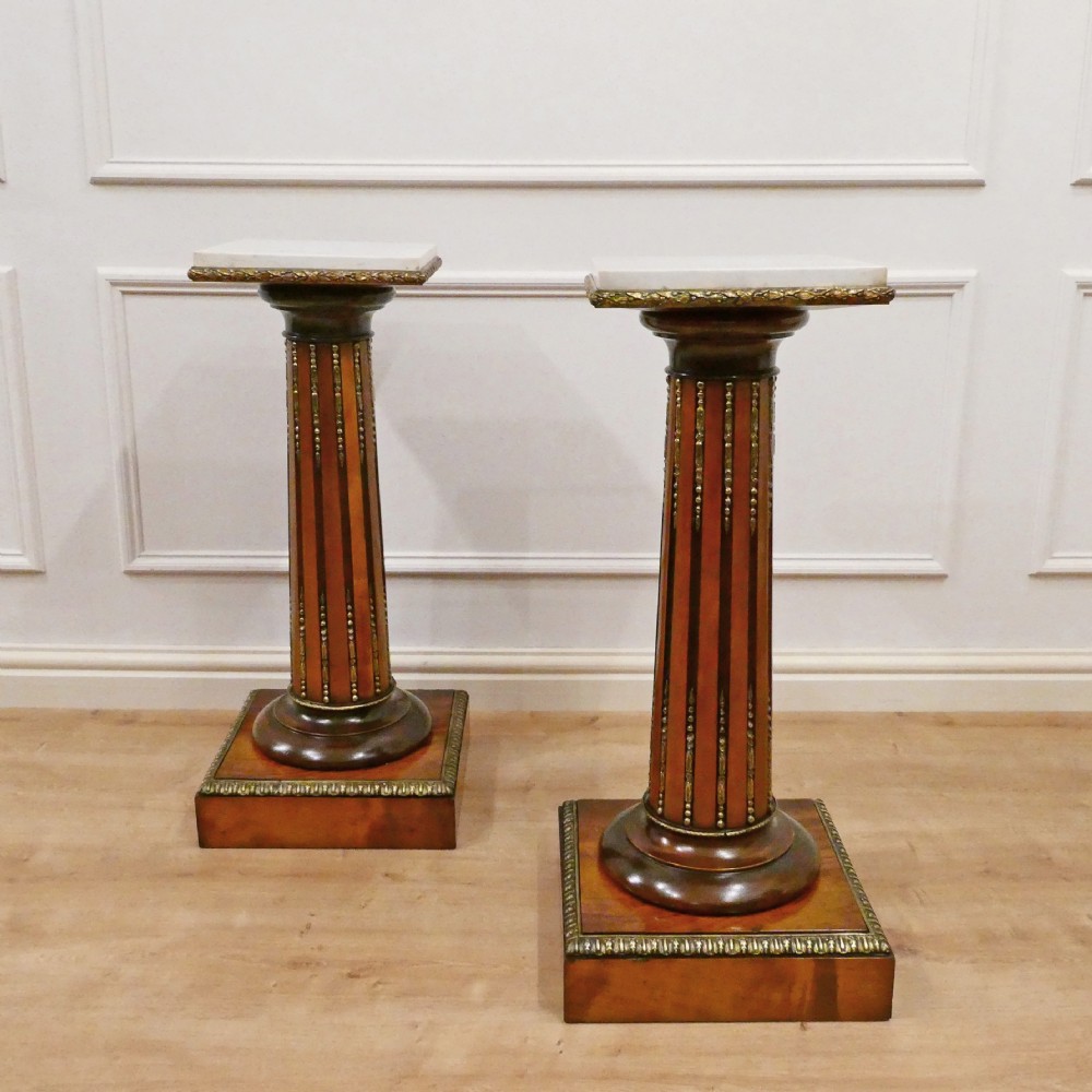 A pair of Victorian fluted satinwood column pedestals with square white marble tops and gilt mounts on plinth bases.
