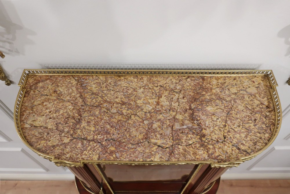 French Louis XVI style mahogany and ormolu-mounted vitrine cabinet featuring curved glass sides, a mirrored back interior, glass shelves, and a marble tier below fluted legs. View IV