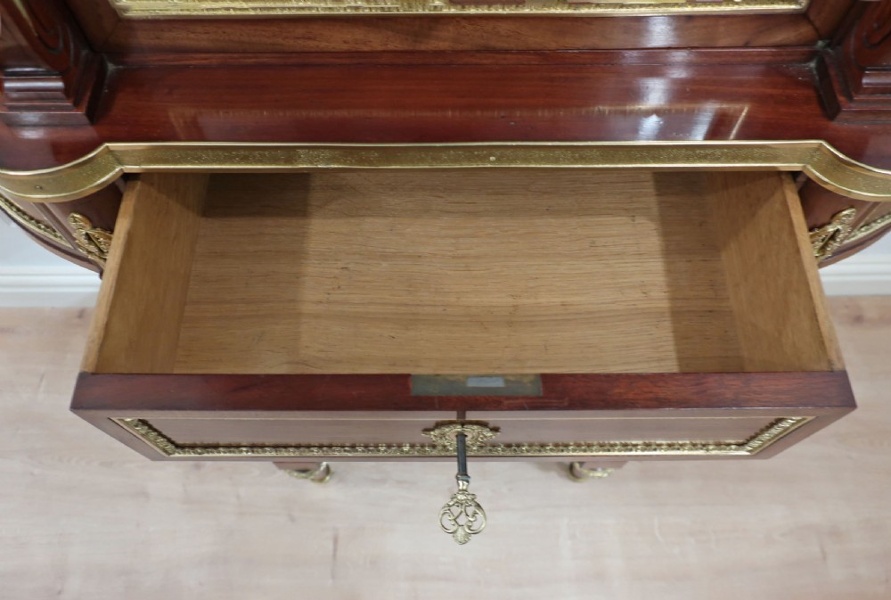 French Louis XVI style mahogany and ormolu-mounted vitrine cabinet featuring curved glass sides, a mirrored back interior, glass shelves, and a marble tier below fluted legs. View VII