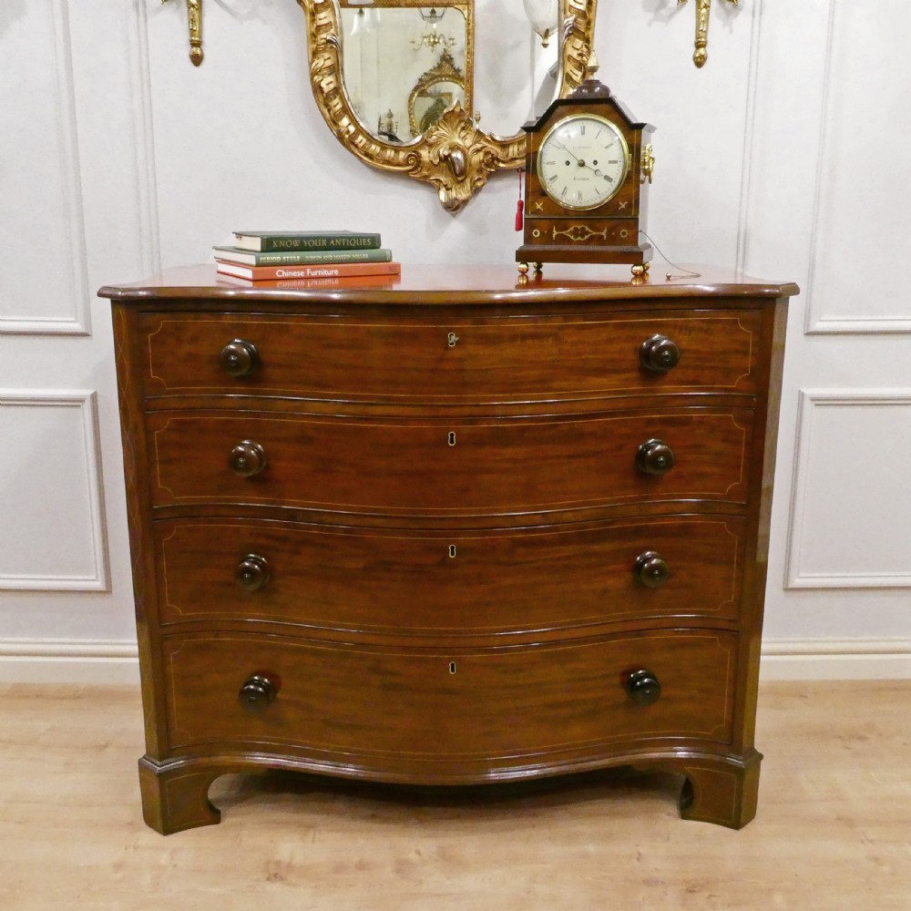 A Georgian mahogany chest of drawers featuring a serpentine front, four graduated drawers with turned wooden knobs, fine line inlay, and bracket feet.