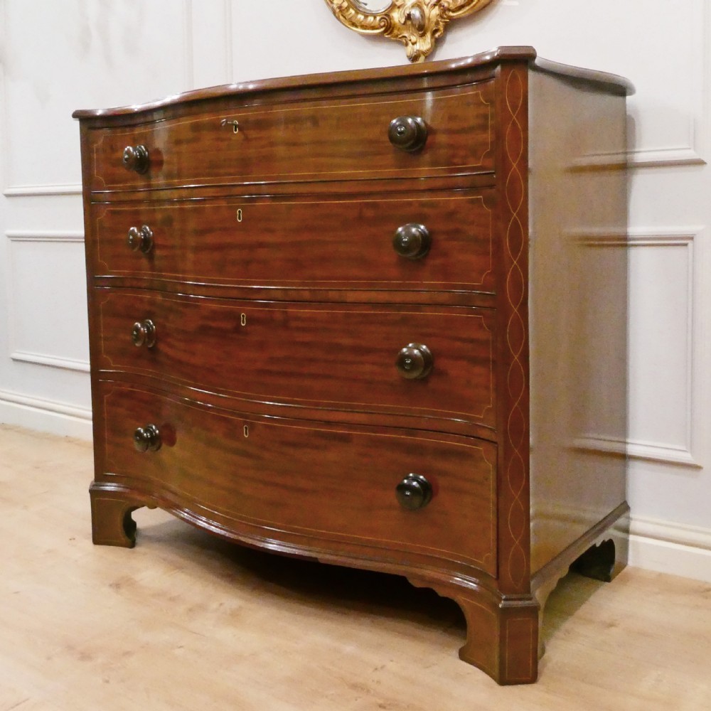 A Georgian mahogany chest of drawers featuring a serpentine front, four graduated drawers with turned wooden knobs, fine line inlay, and bracket feet. View II