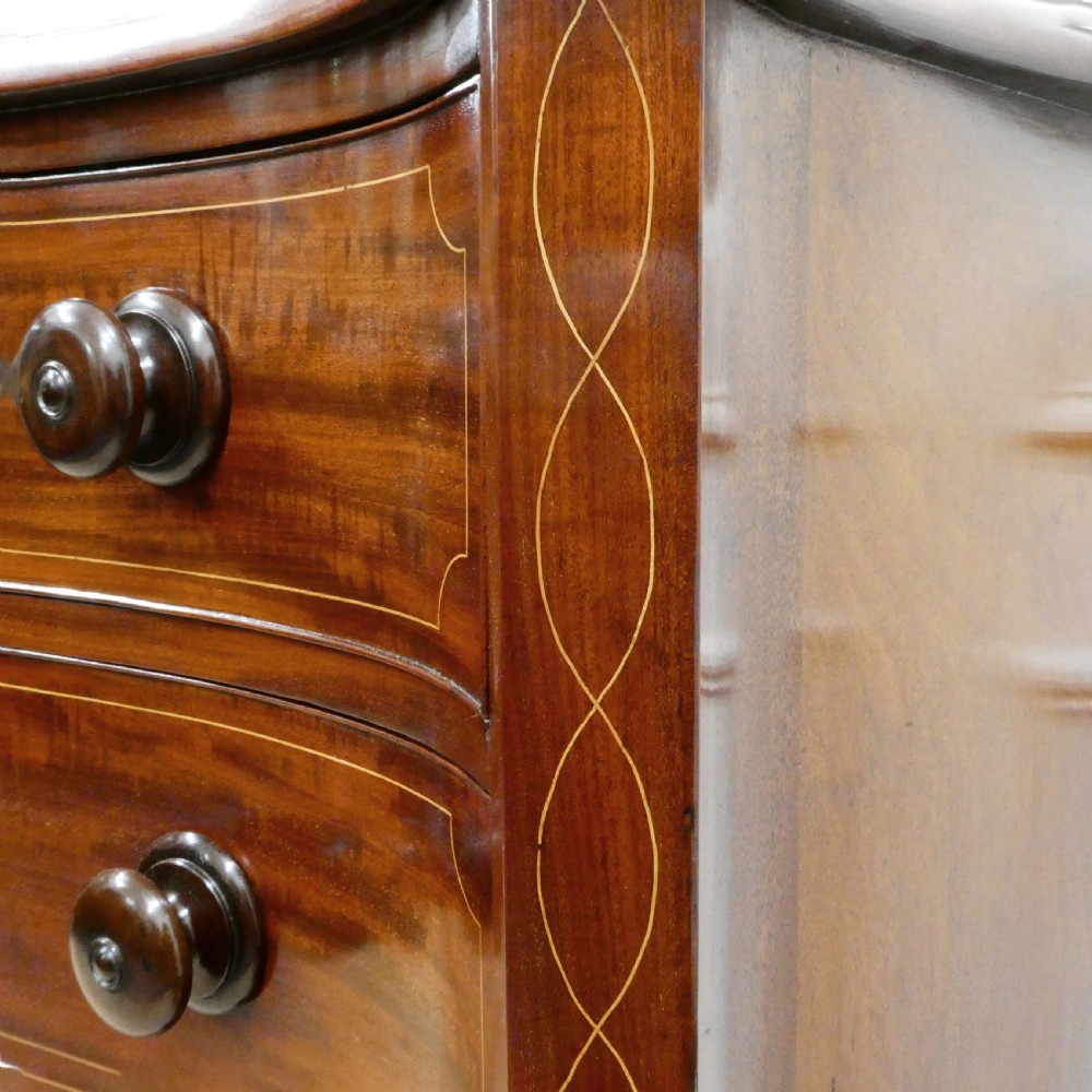 A Georgian mahogany chest of drawers featuring a serpentine front, four graduated drawers with turned wooden knobs, fine line inlay, and bracket feet. View IV