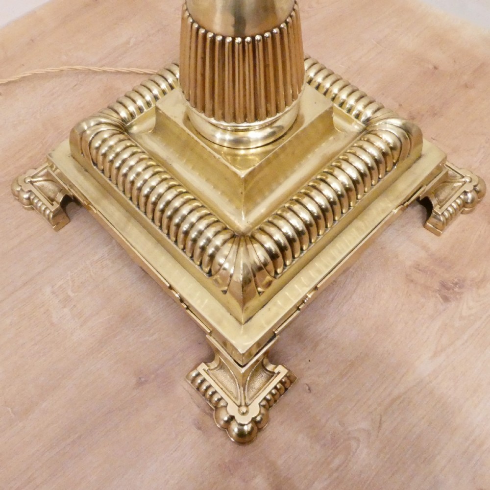 A tall Victorian brass standard lamp featuring a fluted column, tiered square base, and a domed gold silk shade trimmed with beaded fringe and red tassels. View IV