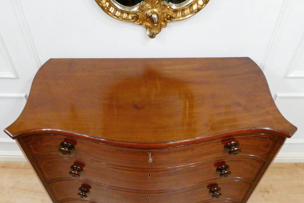 A Georgian mahogany chest of drawers featuring a serpentine front, four graduated drawers with turned wooden knobs, fine line inlay, and bracket feet. View V